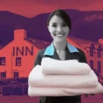 A friendly hotel staff member holding fresh towels in front of a budget inn and suites nestled in a hilly landscape