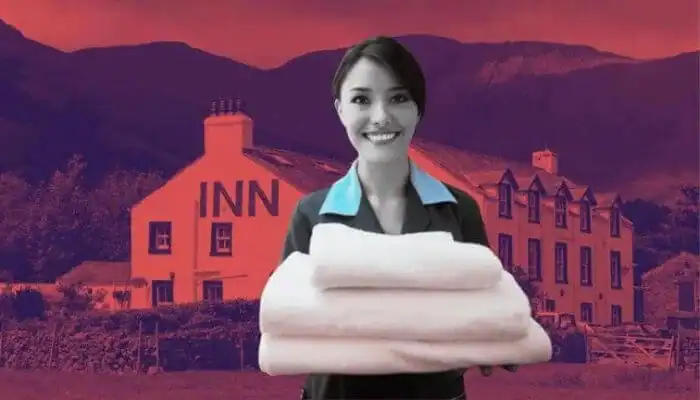 A friendly hotel staff member holding fresh towels in front of a budget inn and suites nestled in a hilly landscape